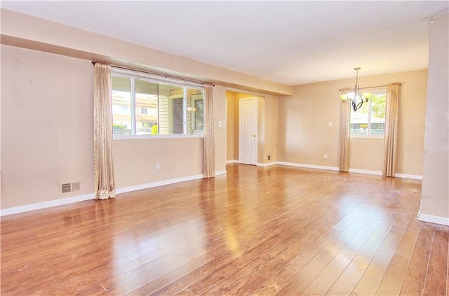 empty room with baseboards, visible vents, light wood-type flooring, and a notable chandelier