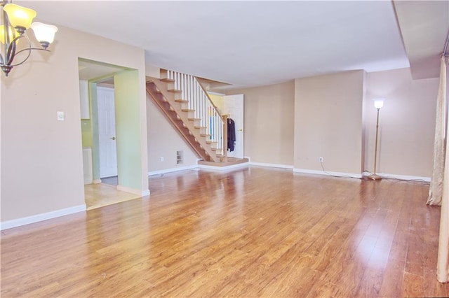 unfurnished living room featuring baseboards, light wood-style flooring, a notable chandelier, and stairway