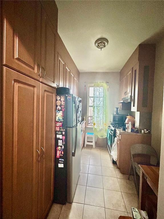 kitchen with under cabinet range hood, appliances with stainless steel finishes, and light tile patterned floors