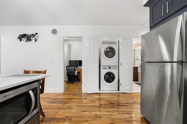 laundry area featuring baseboards, light wood finished floors, and stacked washer and dryer