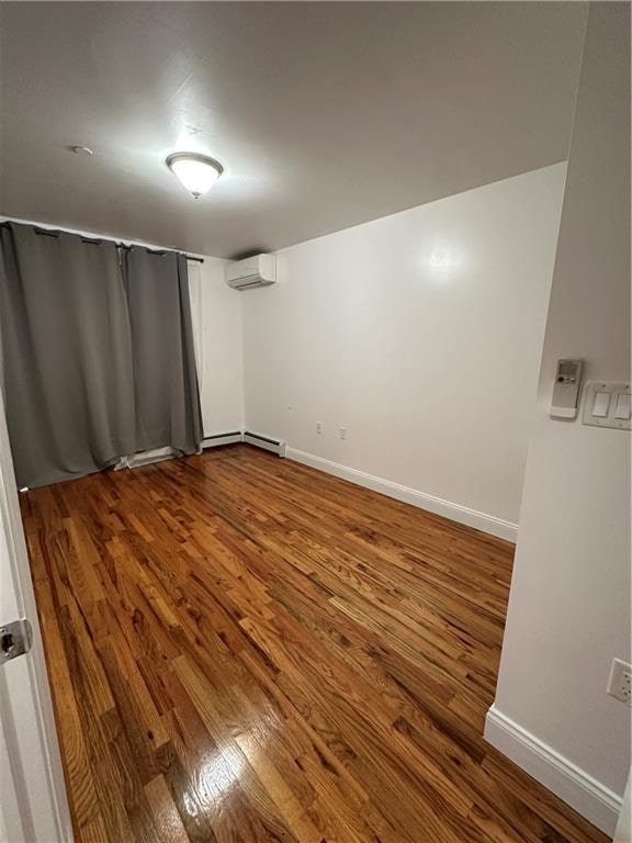 spare room featuring baseboards, a wall mounted air conditioner, a baseboard heating unit, and wood finished floors