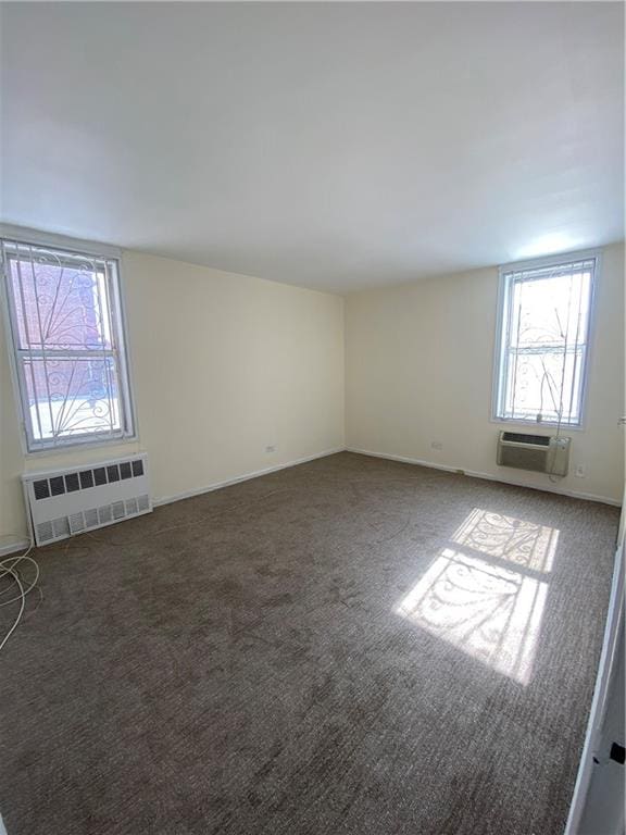 carpeted empty room featuring radiator heating unit, baseboards, and a wall unit AC