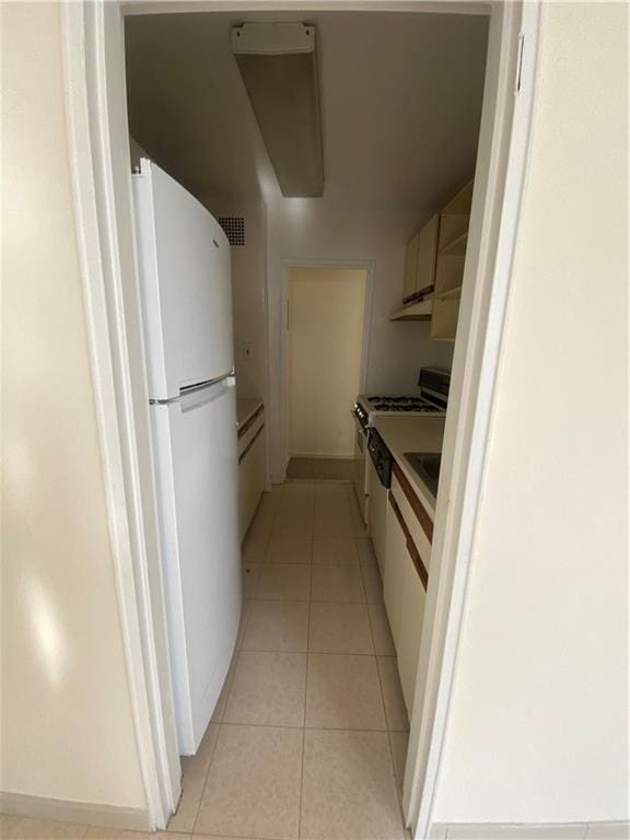 kitchen featuring gas range, light tile patterned floors, freestanding refrigerator, under cabinet range hood, and white cabinetry