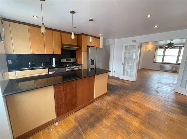 kitchen with dark countertops, appliances with stainless steel finishes, a sink, dark wood finished floors, and under cabinet range hood