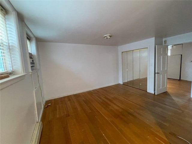 unfurnished bedroom with a closet, baseboards, wood finished floors, and baseboard heating