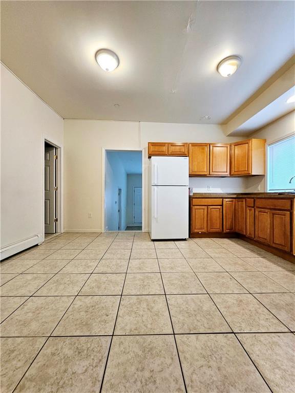 kitchen featuring freestanding refrigerator, brown cabinetry, light tile patterned floors, and a baseboard radiator