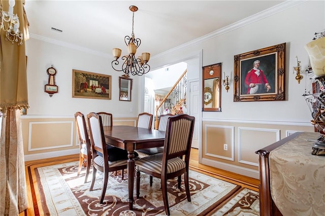 dining area with crown molding, an inviting chandelier, a wainscoted wall, light wood-type flooring, and visible vents