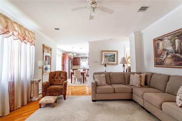 living room featuring visible vents, ornamental molding, light wood-style flooring, and ceiling fan with notable chandelier