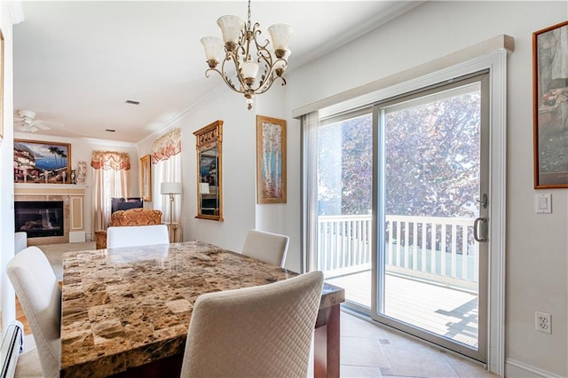 dining space with crown molding, a glass covered fireplace, baseboard heating, ceiling fan with notable chandelier, and light tile patterned floors