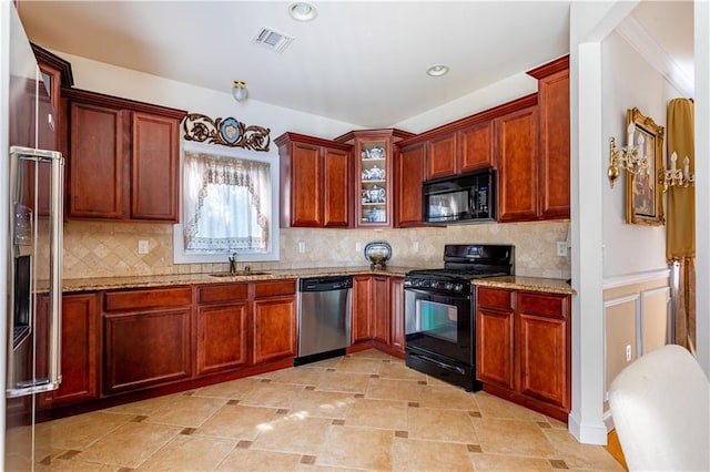 kitchen with visible vents, a sink, light stone counters, black appliances, and glass insert cabinets