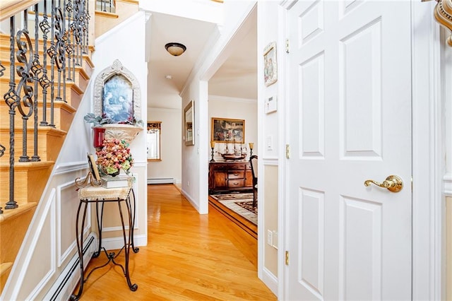 corridor with crown molding, a baseboard heating unit, stairway, and light wood-type flooring