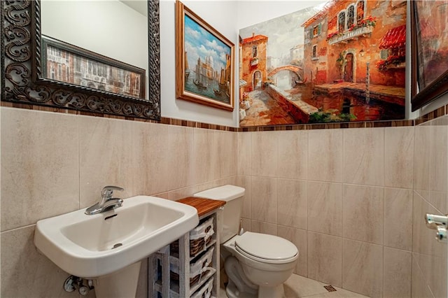 bathroom featuring a sink, a wainscoted wall, toilet, and tile walls
