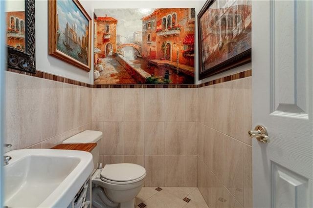 bathroom featuring tile patterned flooring, a sink, toilet, and tile walls
