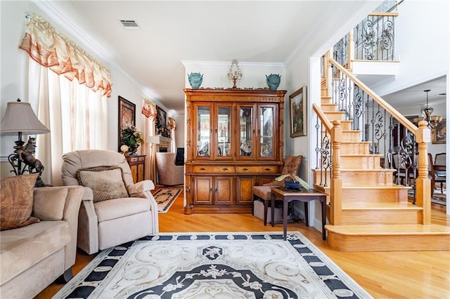 living room featuring visible vents, ornamental molding, light wood finished floors, and stairway