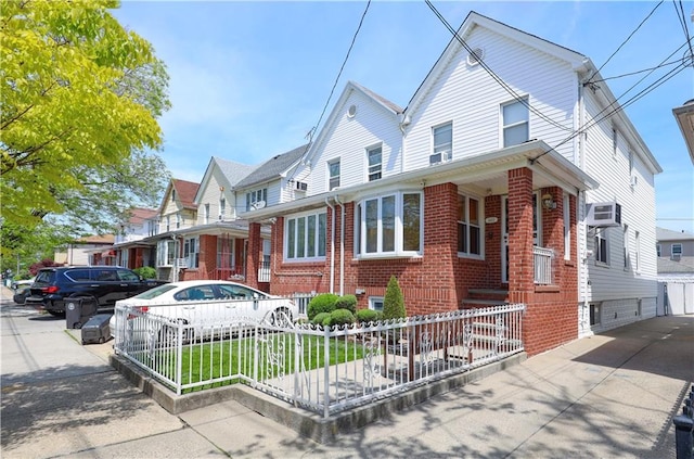 view of front facade featuring brick siding, a residential view, a fenced front yard, and a wall mounted air conditioner