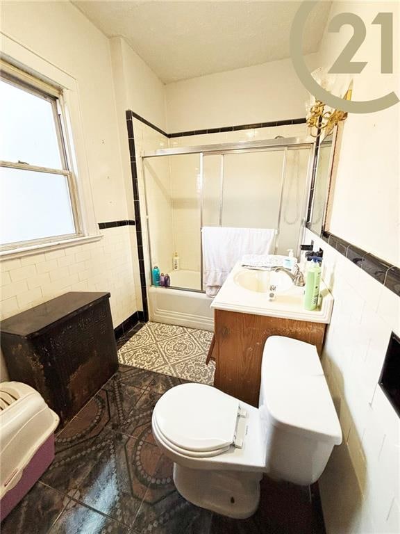 1817 E 15th St, Brooklyn, NY 11229 - bathroom featuring toilet, bath / shower combo with glass door, a wainscoted wall, vanity, and tile walls