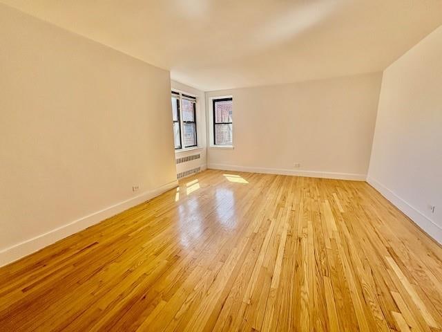 unfurnished room featuring light wood-style floors, radiator, and baseboards