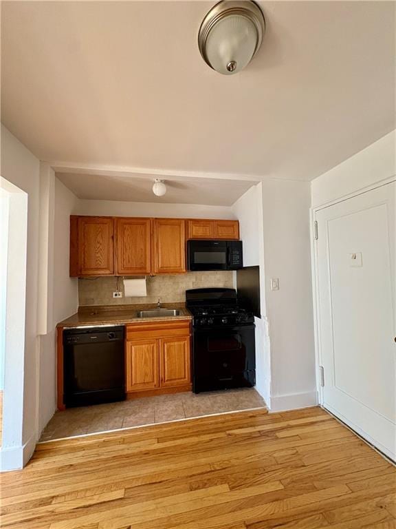 kitchen with brown cabinets, a sink, black appliances, and light wood-type flooring