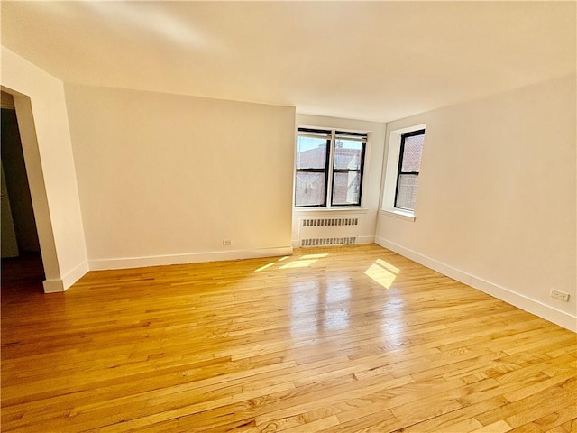 spare room featuring radiator heating unit, baseboards, and light wood finished floors