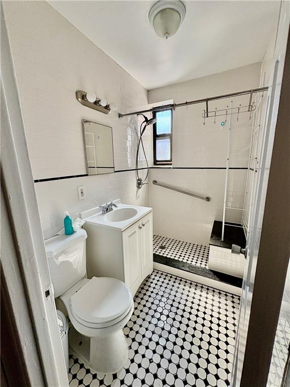bathroom featuring vanity, a shower stall, toilet, and tile walls