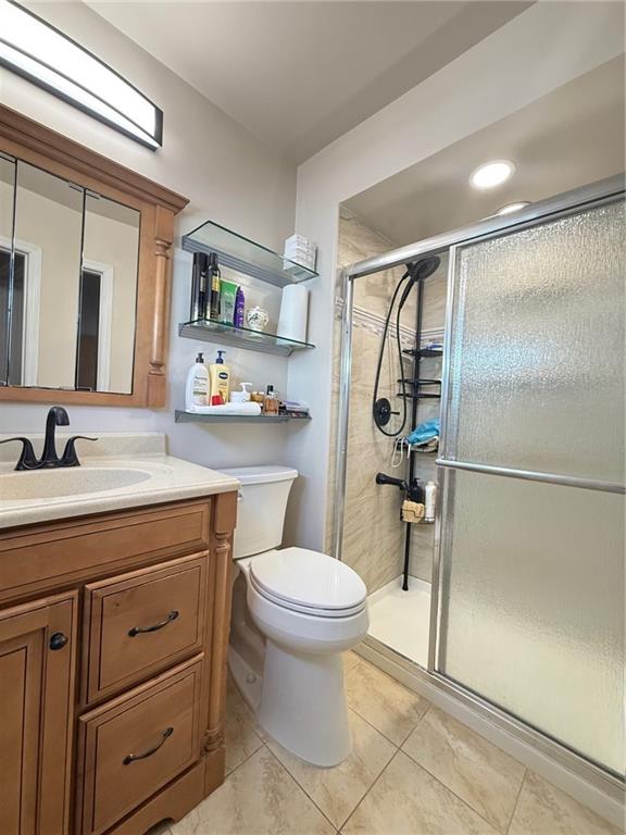 bathroom featuring vanity, toilet, tile patterned flooring, and a stall shower
