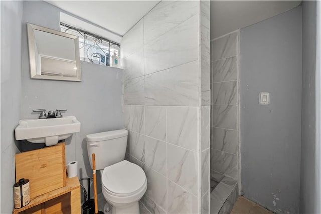 bathroom featuring a sink, a tile shower, toilet, and tile walls