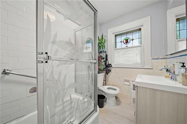 full bath featuring toilet, tile walls, combined bath / shower with glass door, and vanity