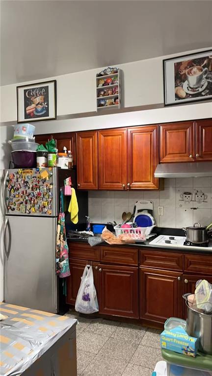 kitchen with tasteful backsplash, freestanding refrigerator, under cabinet range hood, and granite finish floor