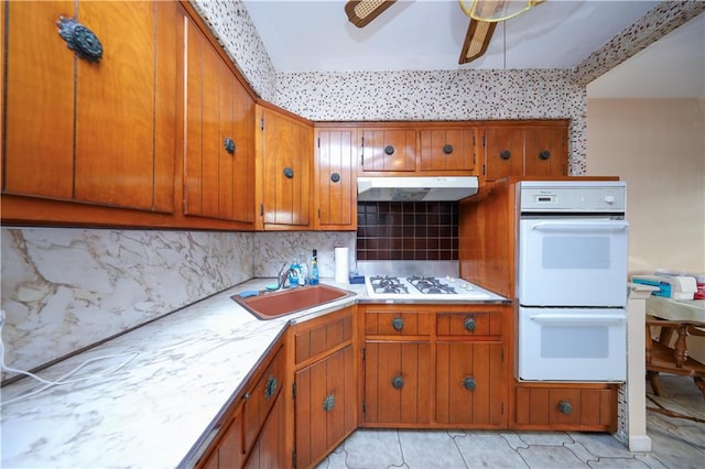 kitchen with brown cabinets, a sink, white appliances, light countertops, and under cabinet range hood