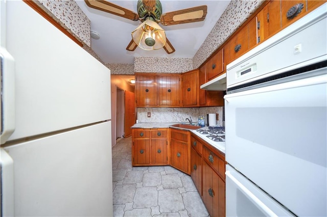 kitchen with light countertops, a sink, brown cabinets, and white appliances