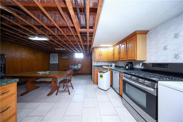 kitchen with dark countertops, wooden walls, brown cabinets, appliances with stainless steel finishes, and light tile patterned floors