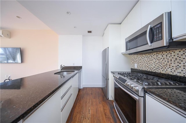 kitchen featuring white cabinets, appliances with stainless steel finishes, a sink, and dark stone counters