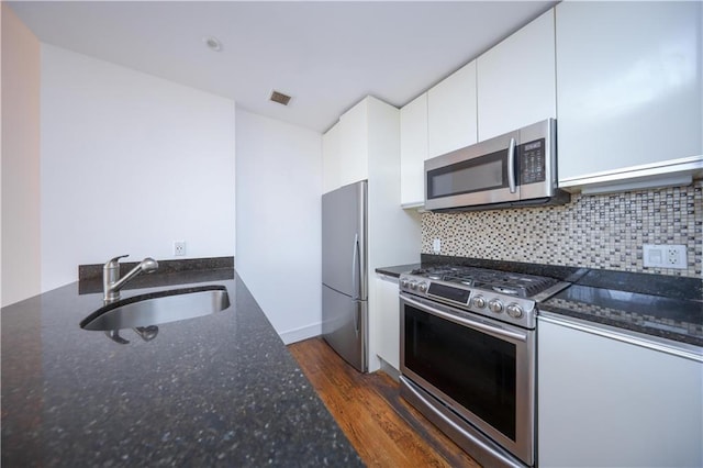 kitchen with a sink, dark stone counters, stainless steel appliances, and white cabinetry