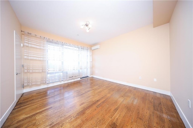 unfurnished room featuring baseboards, an AC wall unit, and wood finished floors