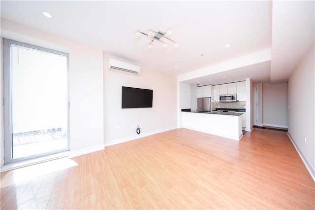 unfurnished living room featuring light wood-style floors, baseboards, a wall mounted air conditioner, and a wealth of natural light