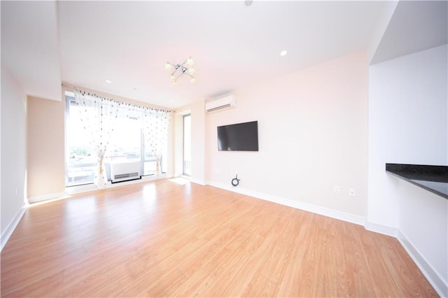 unfurnished living room with an AC wall unit, baseboards, and light wood finished floors