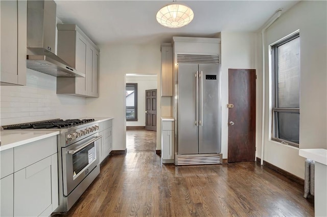 kitchen featuring decorative backsplash, high end appliances, dark wood-type flooring, light countertops, and wall chimney exhaust hood