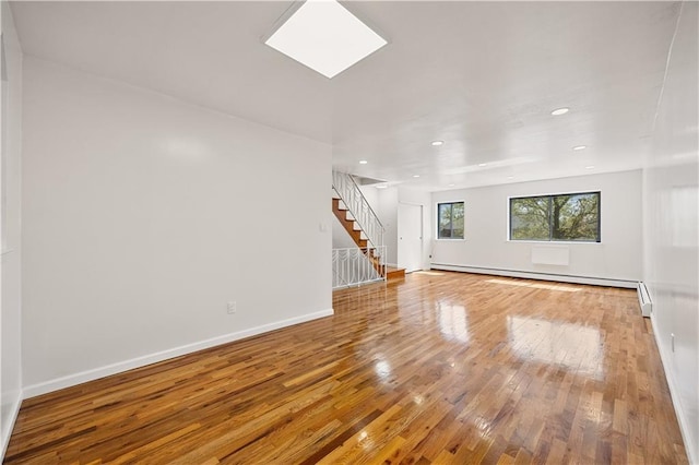 unfurnished living room featuring baseboards, stairs, baseboard heating, and wood finished floors