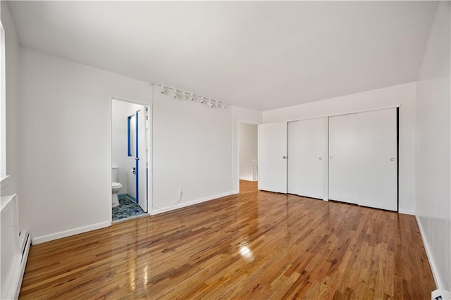 unfurnished bedroom featuring a closet, baseboards, baseboard heating, and light wood-style floors