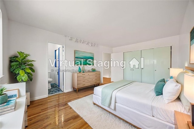 bedroom featuring track lighting, baseboards, wood finished floors, ensuite bathroom, and a closet
