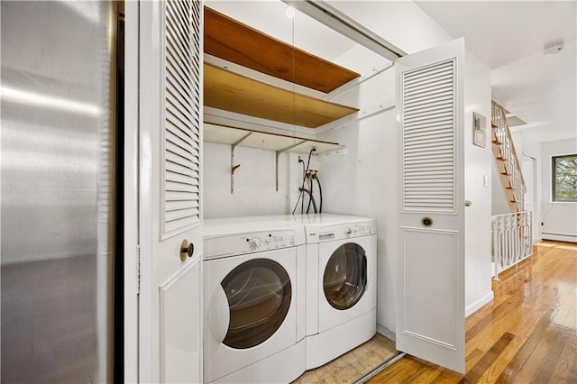 washroom featuring laundry area, light wood finished floors, a baseboard heating unit, and separate washer and dryer
