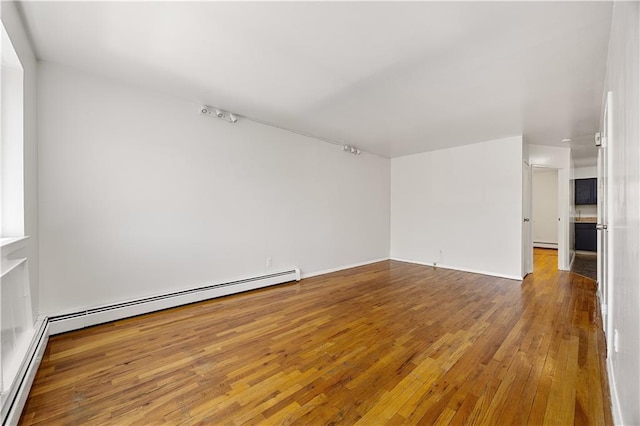 empty room featuring a baseboard radiator, wood-type flooring, and a baseboard heating unit
