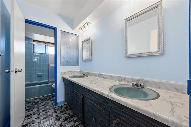 full bath featuring a sink, bath / shower combo with glass door, toilet, and double vanity