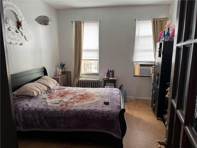 bedroom featuring wood finished floors, radiator heating unit, multiple windows, and cooling unit