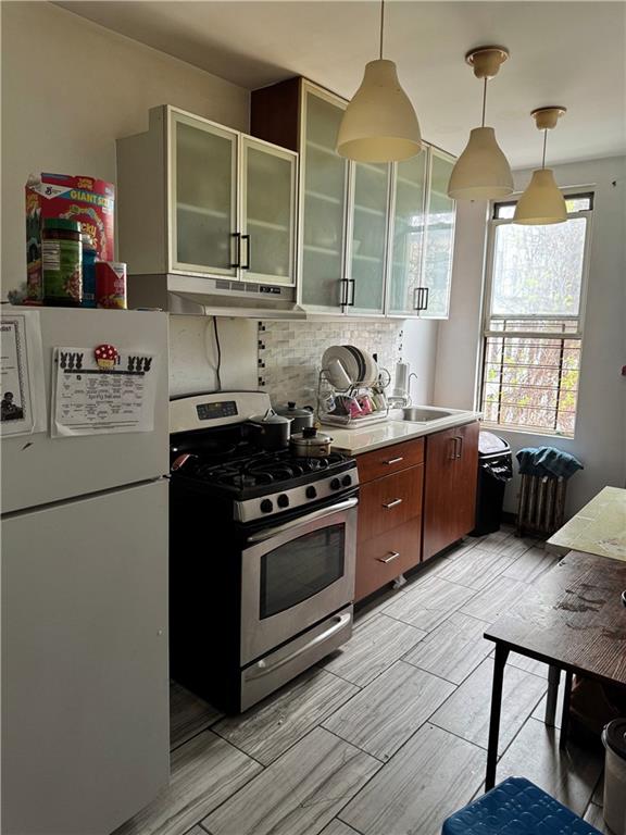 kitchen with freestanding refrigerator, stainless steel gas range, light countertops, under cabinet range hood, and tasteful backsplash