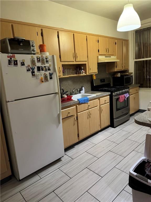 kitchen with freestanding refrigerator, stainless steel gas range, under cabinet range hood, tasteful backsplash, and a sink