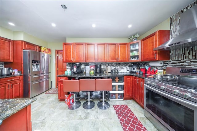 kitchen featuring wall chimney range hood, stainless steel appliances, dark brown cabinets, and tasteful backsplash
