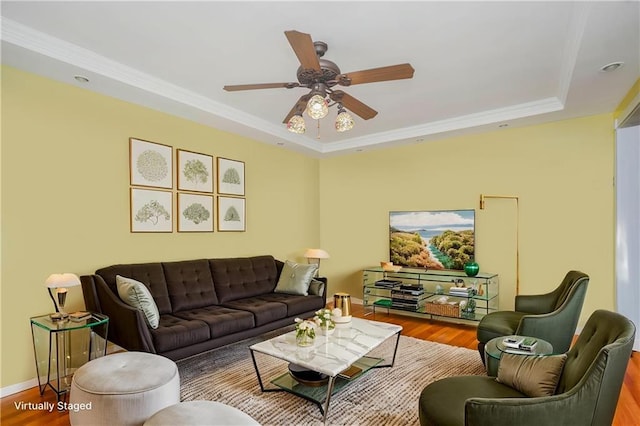 living room featuring ceiling fan, ornamental molding, a tray ceiling, and wood finished floors