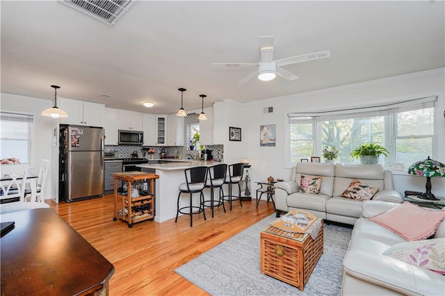 living area with crown molding, ceiling fan, light wood-style flooring, and visible vents