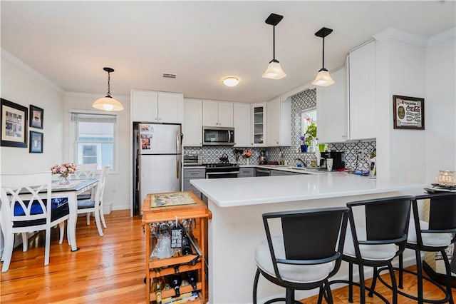 kitchen featuring a peninsula, a breakfast bar, light countertops, backsplash, and stainless steel appliances